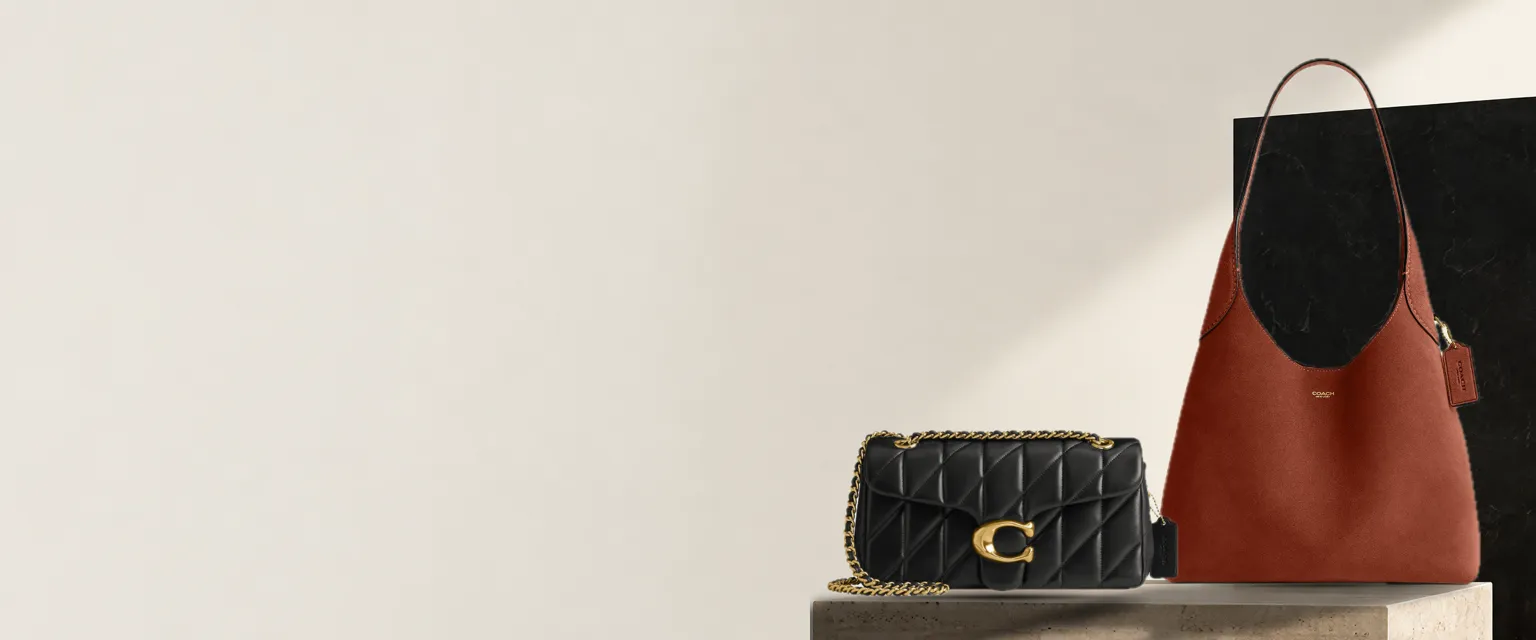 Coach Tabby Shoulder Bag 26 in black quilted leather and Coach Brooklyn Shoulder Bag 28 in rust, on a travertine plinth